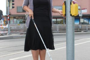Eine junge Dame mit Simulationsbrille und Blindenstock an der Blindenampel. Credit: BSVT