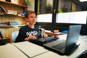 Jakob auf seinem Sitzplatz vor seiner Braillezeile und Laptop