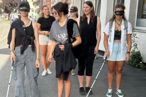Gruppe geht mit Dunkelbrille und Langstock den Weg entlang