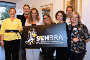 Von links nach rechts: Birgit Brugger, Wolfgang Grünzweig, Eva Pawlata, Sabine Karrer, Katharina Feichtner-Bramböck, Wilhelm Zwirner und Petra Wohlfahrtstätter präsentieren das neue Logo der Frühförderung für Kinder mit Sehbehinderung oder Blindheit (SEHBRA). Foto: ©fotofex2025